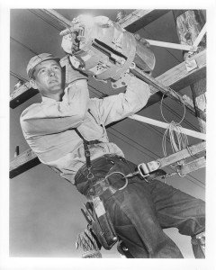 1950s-8 -
Aerial Lineman. The barrel-like object which the lineman placed on the aerial cable performs an operation known as a cable lashing.